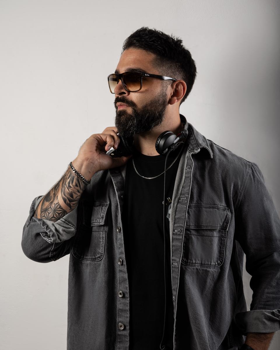 KHALDERA in a grey denim shirt and sunglasses, headphones around his neck